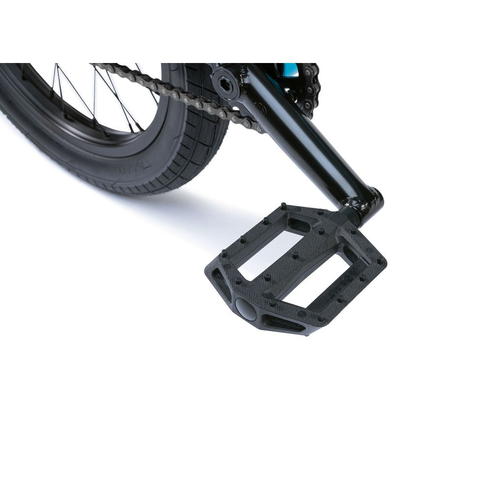 Close-up of a Wethepeople Seed 16 Inch Bike pedal and rear tire, capturing the BMX essence. The black pedal with metal pins is securely attached to a sleek black crank arm.