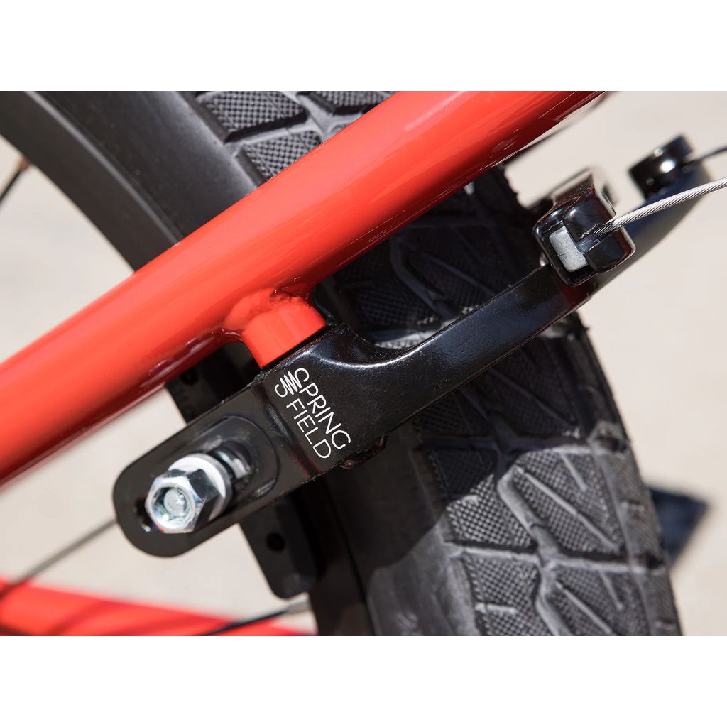 Close-up of Odyssey Springfield brakes labeled "SPRINGFIELD," attached to a red Sunday Primer 18 Inch Bike (2025) frame and a black tire with a textured tread pattern.