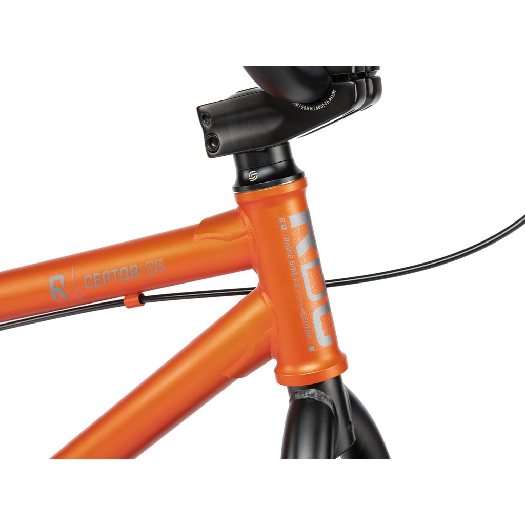 Close-up of an orange bicycle frame labeled "Radio 26 Inch Ceptor Bike" and "RIDG." The image shows the handlebar stem and part of the frame's top tube and down tube, highlighting its robust design ideal for a 26-inch BMX bike.