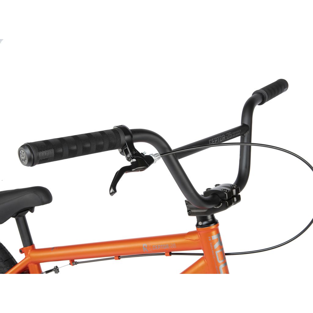 Close-up of the handlebar and brake lever of an orange Radio 26 Inch Ceptor Bike, showing the grips, lever, and part of the frame.