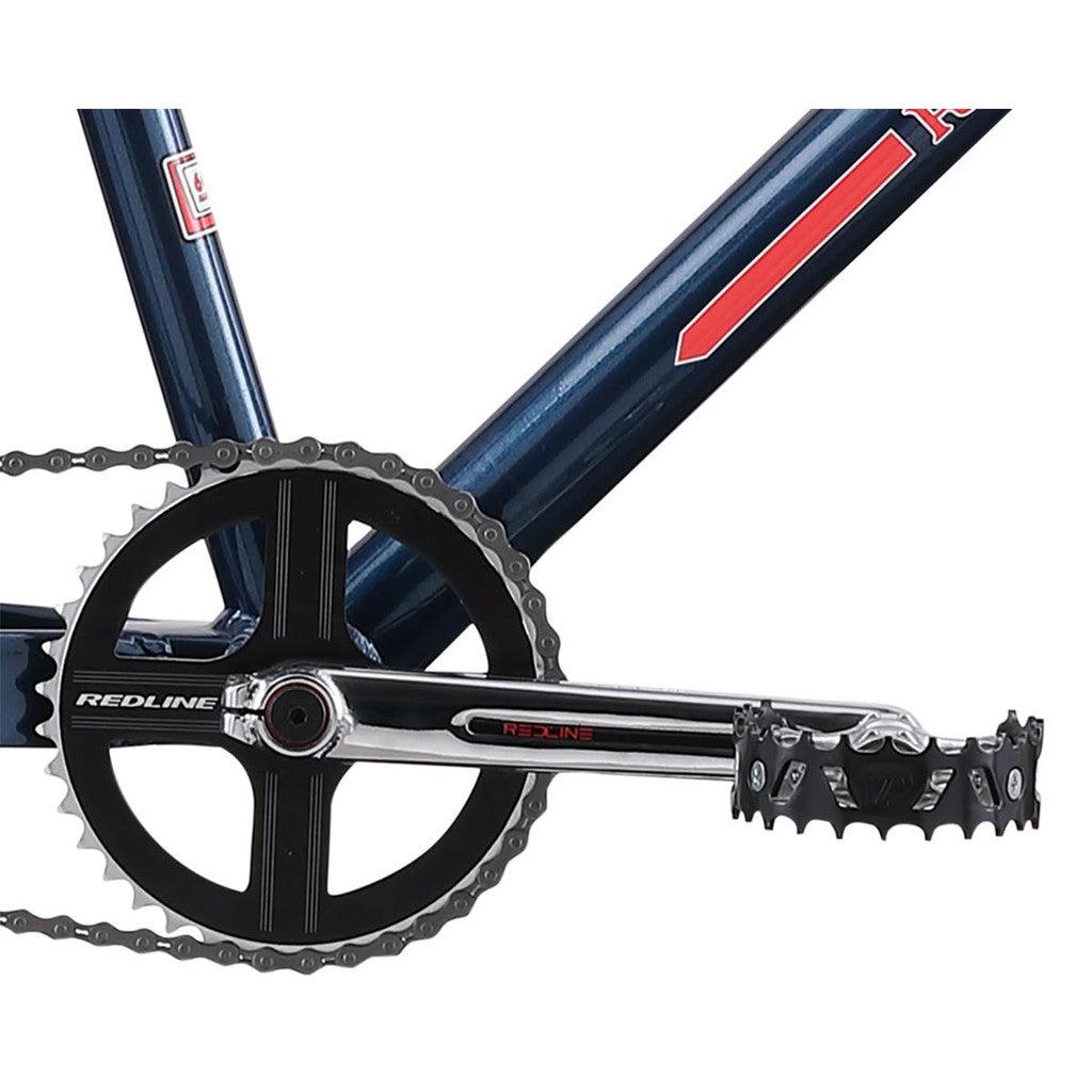 A close-up of the crankset and pedal on a dark blue frame with red and white accents, evoking the sleek design of the Redline SQB 26 Inch Bike.