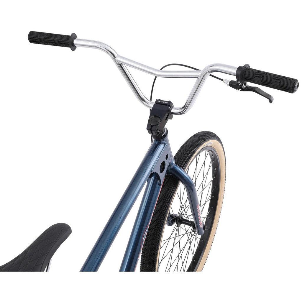 Close-up of the front section of the Redline SQB 26 Inch Bike, highlighting the handlebars, brake lever, and front wheel. This iconic BMX brand showcases its Squareback design with a metallic blue frame and tires featuring beige sidewalls.