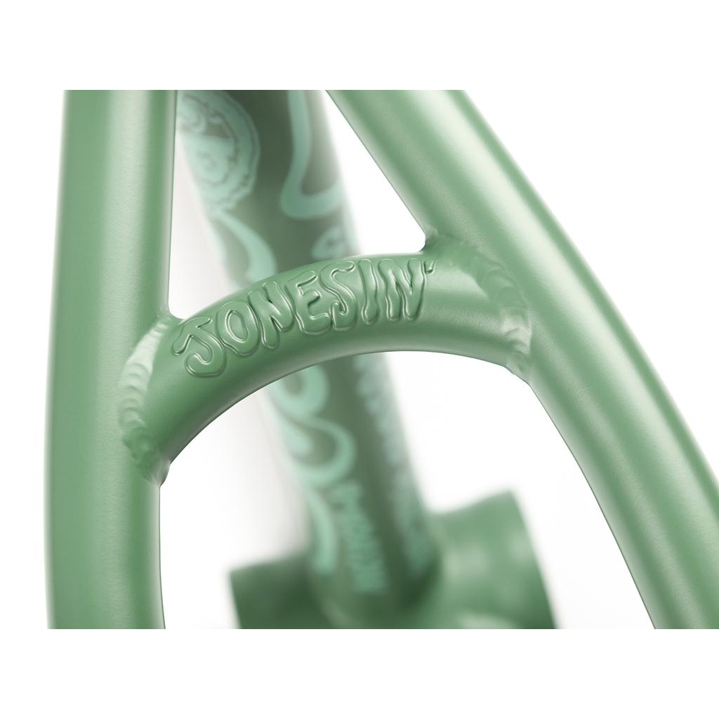 Close-up of a green metal structure embossed with "JONESIN'," resembling the sleek style of the BSD Jonesin Frame (2021). Swirled patterns in the background evoke modern street geometry.