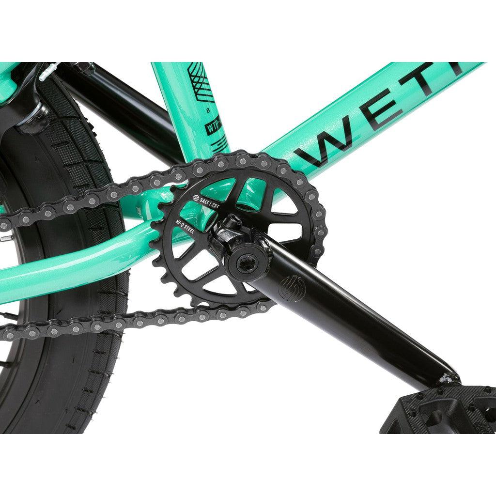 A close-up of a teal bicycle frame showcasing the chain, black crank, and pedals highlights the Wethepeople CRS FS 18 Inch BMX bike with its Salt rotor setup.