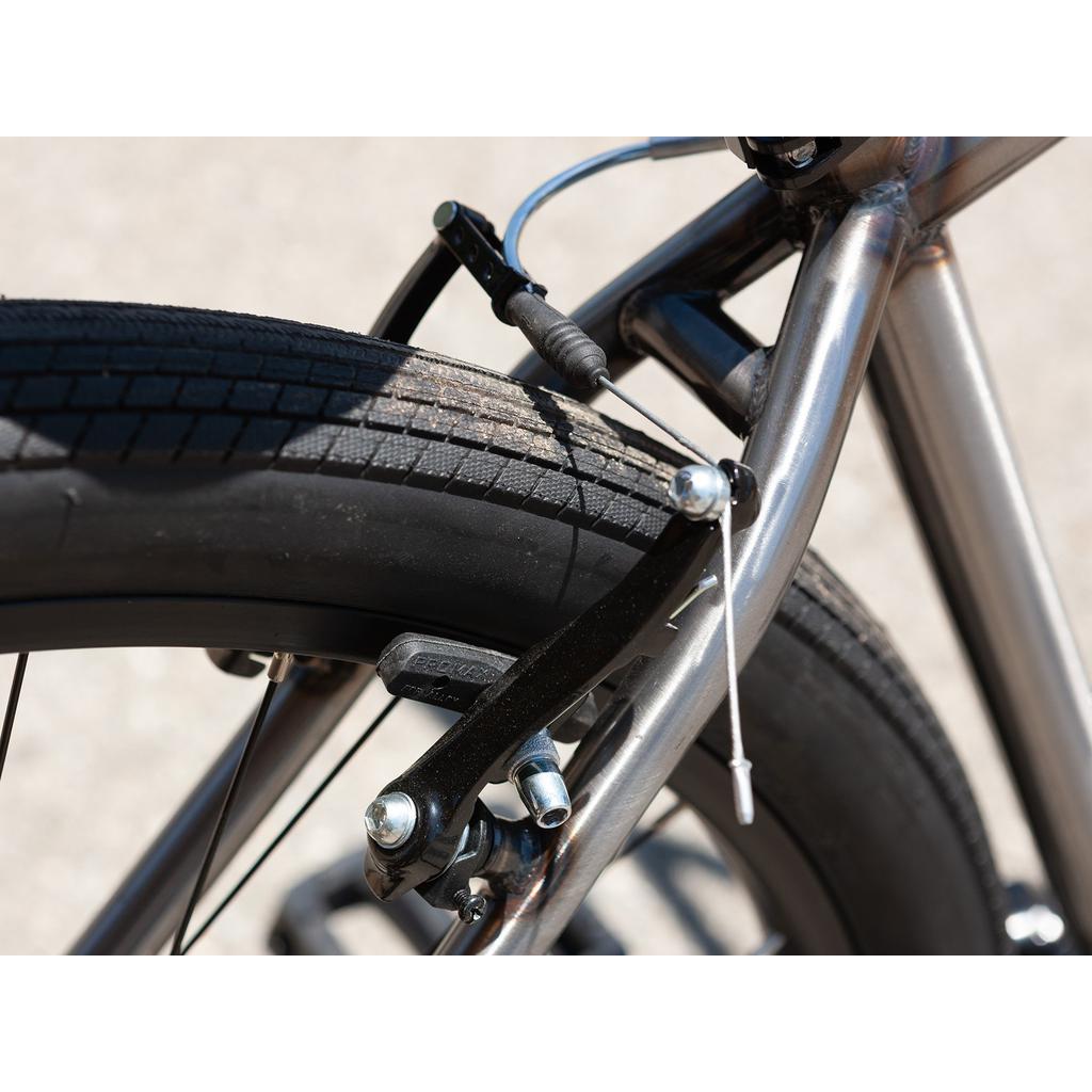 Close-up of the Sunday High C 29 Inch Bike's rear tire and brake system, showcasing its intricate brake pads, cable, and detailed tread pattern.