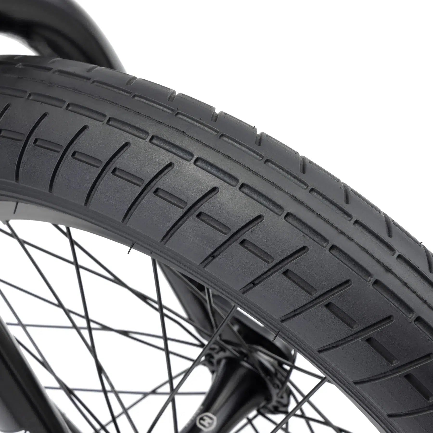 Close-up of a BMX bike tire from the Kink Carve 16 Inch Bike, showcasing a tread pattern along with visible spokes and part of the wheel, echoing the durable design typical of Mission parts.