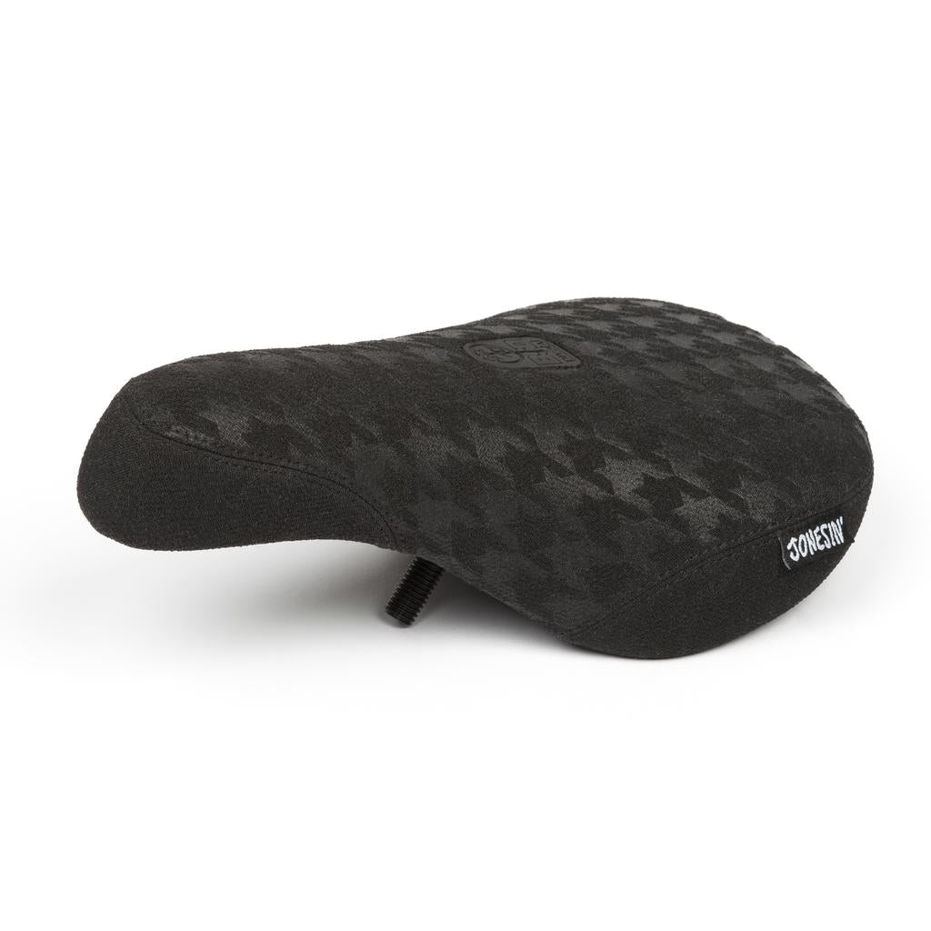 The BSD Jonesin Pivotal Seat is a black bicycle seat with a houndstooth pattern, visible bottom mounting bolt, and Kevlar bumpers for enhanced durability.