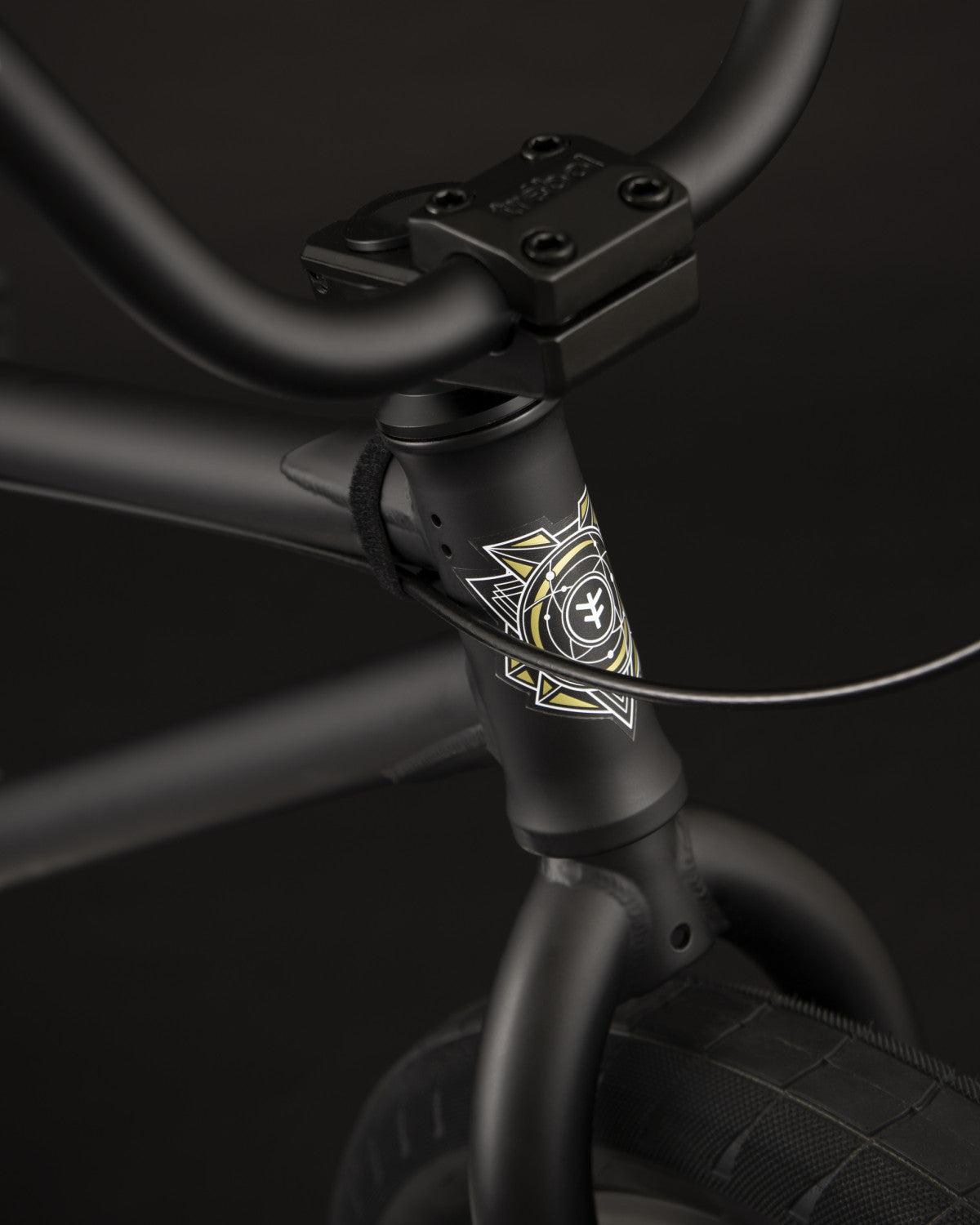 Close-up of a Fly Bikes Electron 20 Inch Bike's black matte handlebar and frame, showcasing a geometric emblem and intricate cable detailing, all crafted with Cr-Mo material for durability.