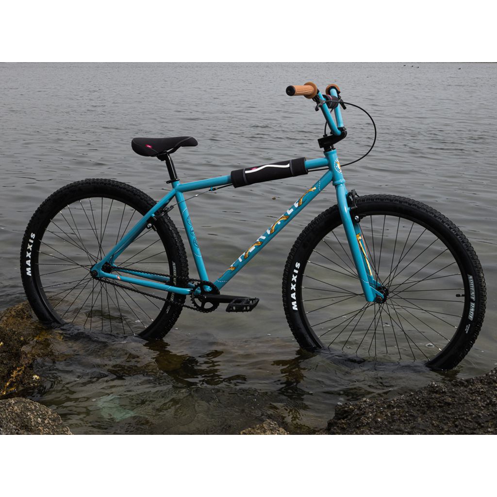 A Fairdale Taj X Vans 27.5 Inch Bike leaning against a rock in the water.