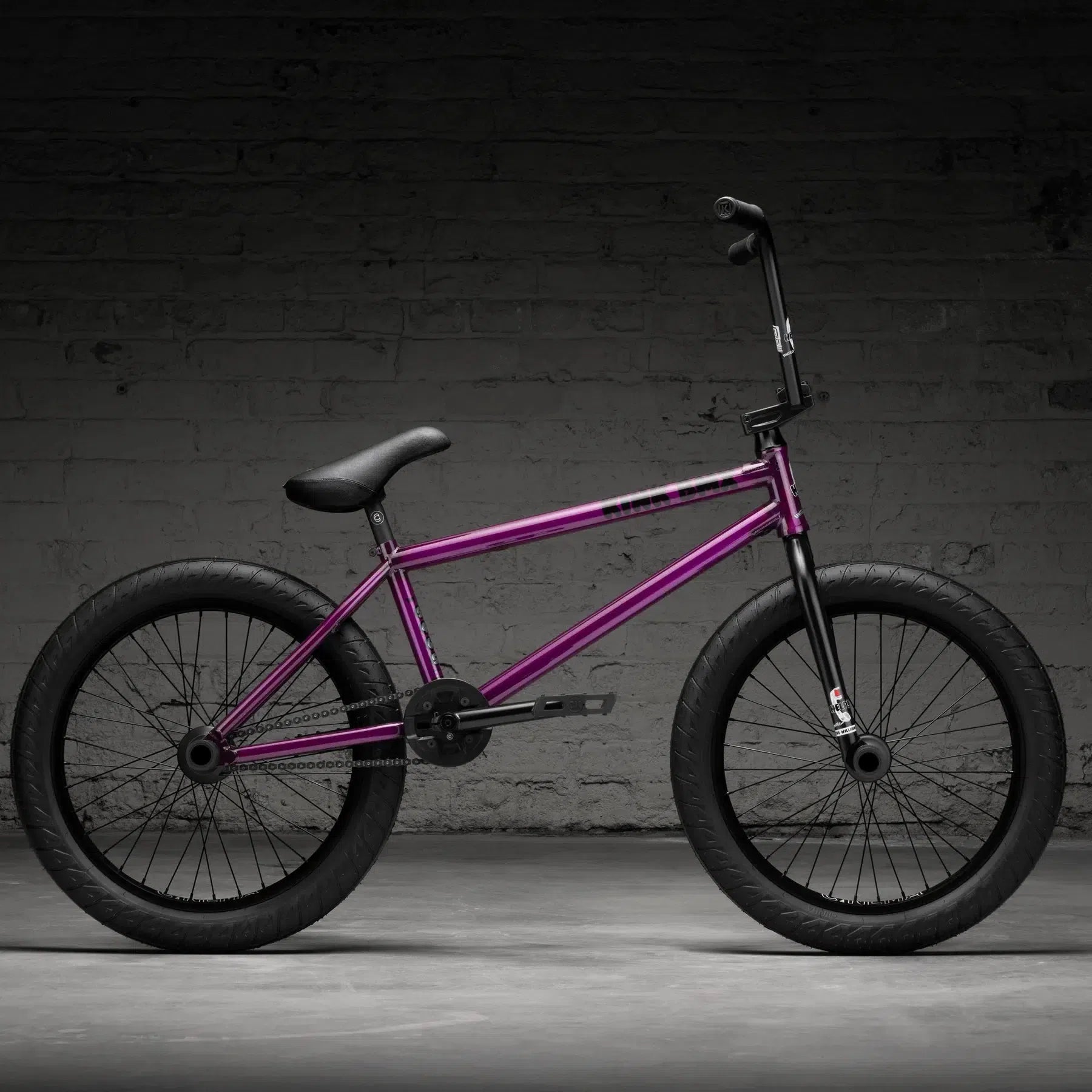 The Kink Williams 20 Inch Bike (2026), a signature ride by Nathan Williams, offers sleek purple aesthetics with black handlebars and tires, beautifully set against a dark brick wall.