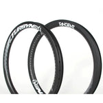 Two black 4K carbon fibre bicycle wheel rims with white branding text, angled side by side against a white background. The lightweight rims are labeled with "Tangent" and "Turbine MX" logos, showcasing the high-quality design of the Tangent Turbyne Carbon Brake Rim 406mm.