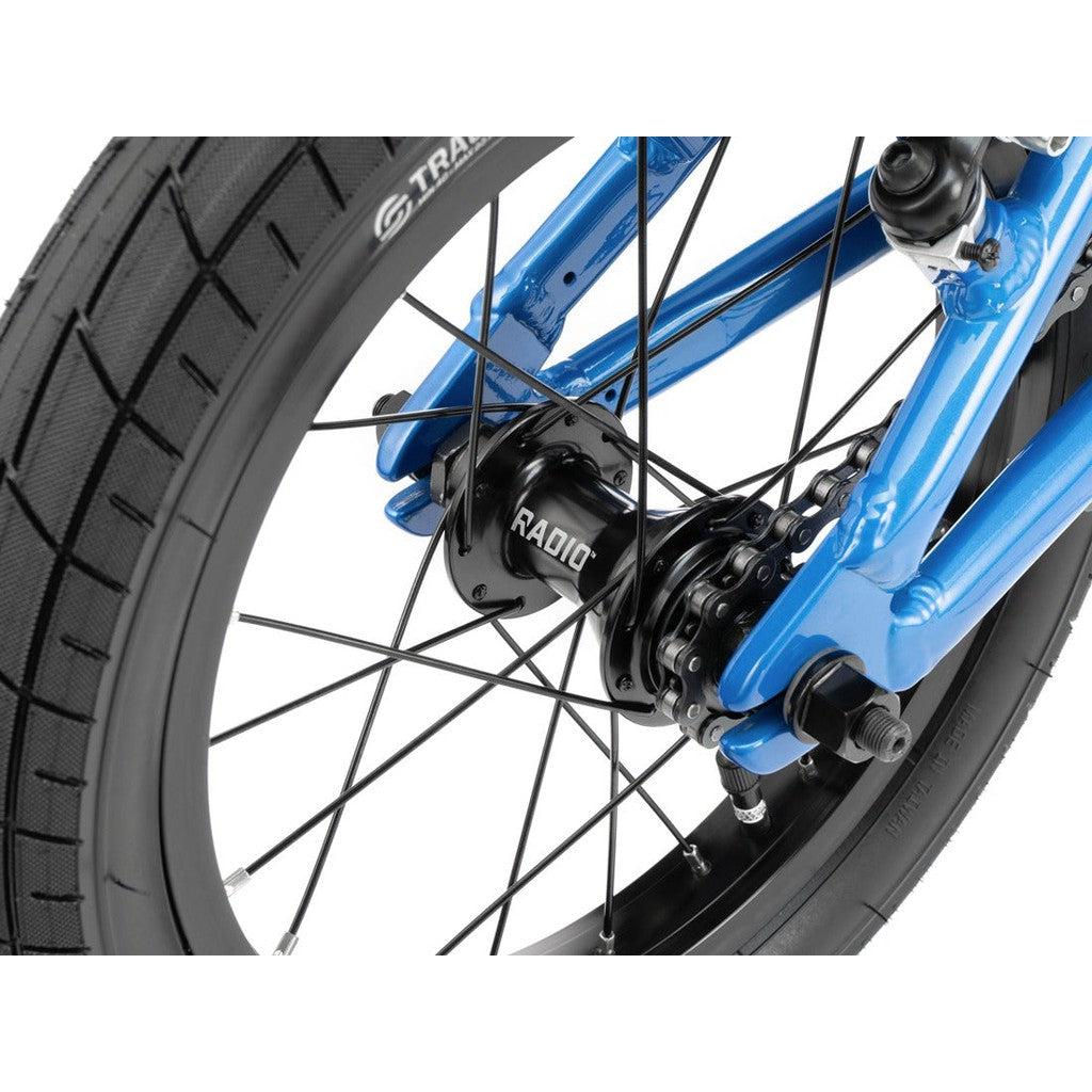 Close-up of the rear wheel of a blue Radio Dice 14 Inch Bike, showcasing the spokes, tire, hub, and part of the 6061-T6 alloy frame. The tire is labeled "Tracer" and the hub is labeled "Radio.