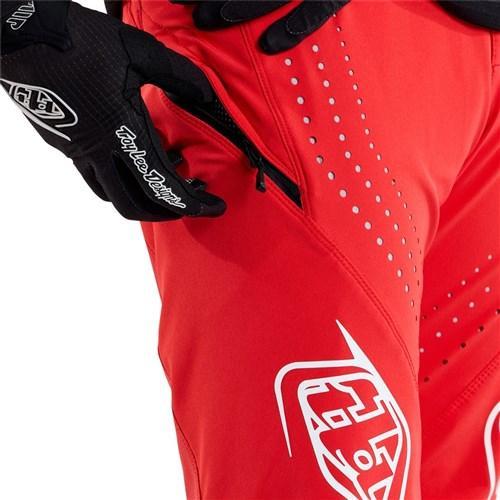 A person adjusts a zippered pocket on the race-ready TLD 25.1 Sprint Pant / Mono Fiery Red while wearing black gloves.