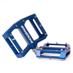 Blue Stay Strong PIVOT Junior Platform Pedals with a flat design and CNC machining for precision. Metallic pins ensure grip, while one pedal stands upright as the other lies flat.