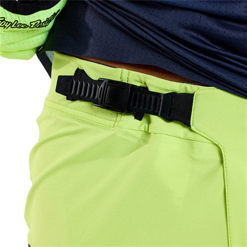 A person wears TLD 25.1 Sprint Ultra Pant in Mono Glow Yellow, crafted with Bluesign-approved fabric, featuring a black adjustable buckle belt for Precision Fit, paired perfectly with a dark jacket.