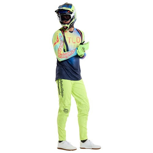 A person in a vibrant motocross outfit, featuring TLD 25.1 Sprint Ultra Pant / Mono Glow Yellow made from Bluesign-approved fabric, with a helmet and gloves, stands neutrally.