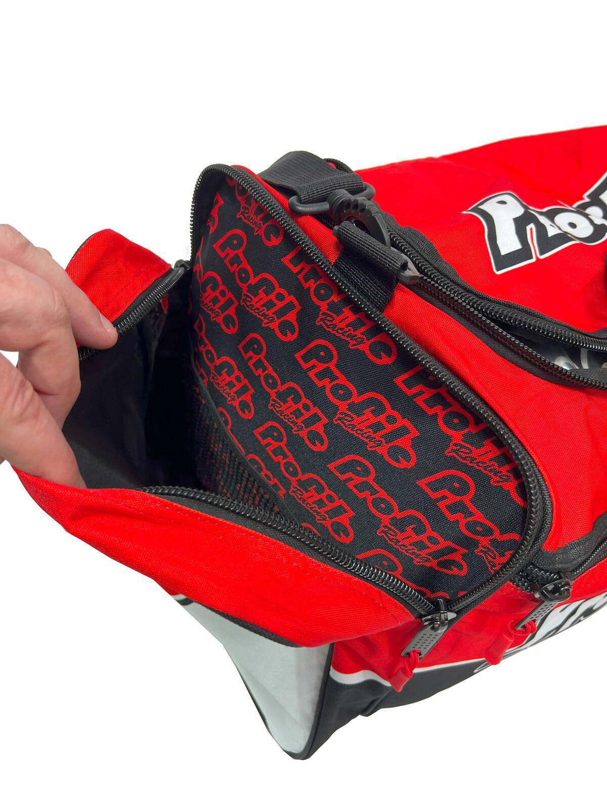 A red and black Profile Racing Custom Team Gear Bag, featuring the "Profig" logo, unzips to show its branded interior. Made from durable 600D polyester with a waterproof lining, it keeps essentials safe. A person's hand grips the zipper.