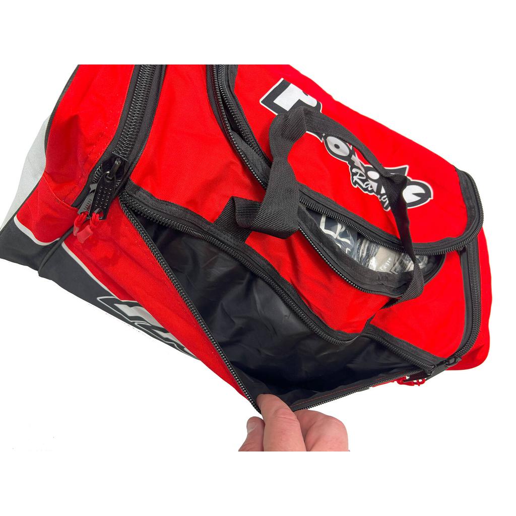 A person holds a Profile Racing Custom Team Gear Bag made from durable 600D polyester. The red and black racing-themed sports bag features an open side pocket, perfect for quick access.