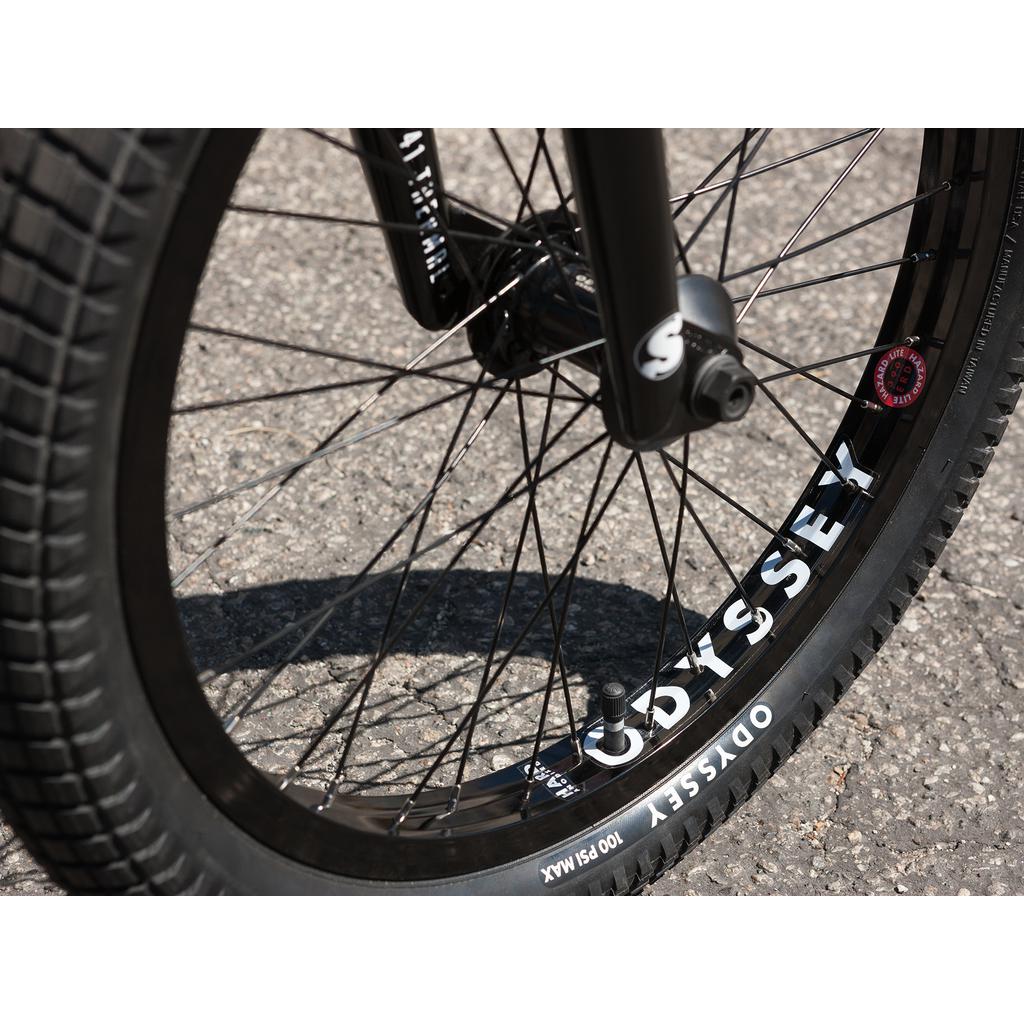 Close-up of a 20-inch bike wheel with black spokes and tire featuring the "Odyssey" label on a paved surface. It perfectly complements the Sunday Wave Length 20 Inch (Gary Young) Bike for cycling enthusiasts.