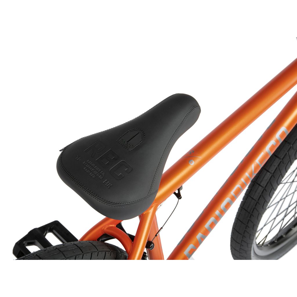 Close-up view of a black bicycle seat attached to an orange frame Radio 26 Inch Ceptor Bike. The seat has the brand name and model inscribed on it, highlighting its precision craftsmanship with sealed bearings for smooth performance.