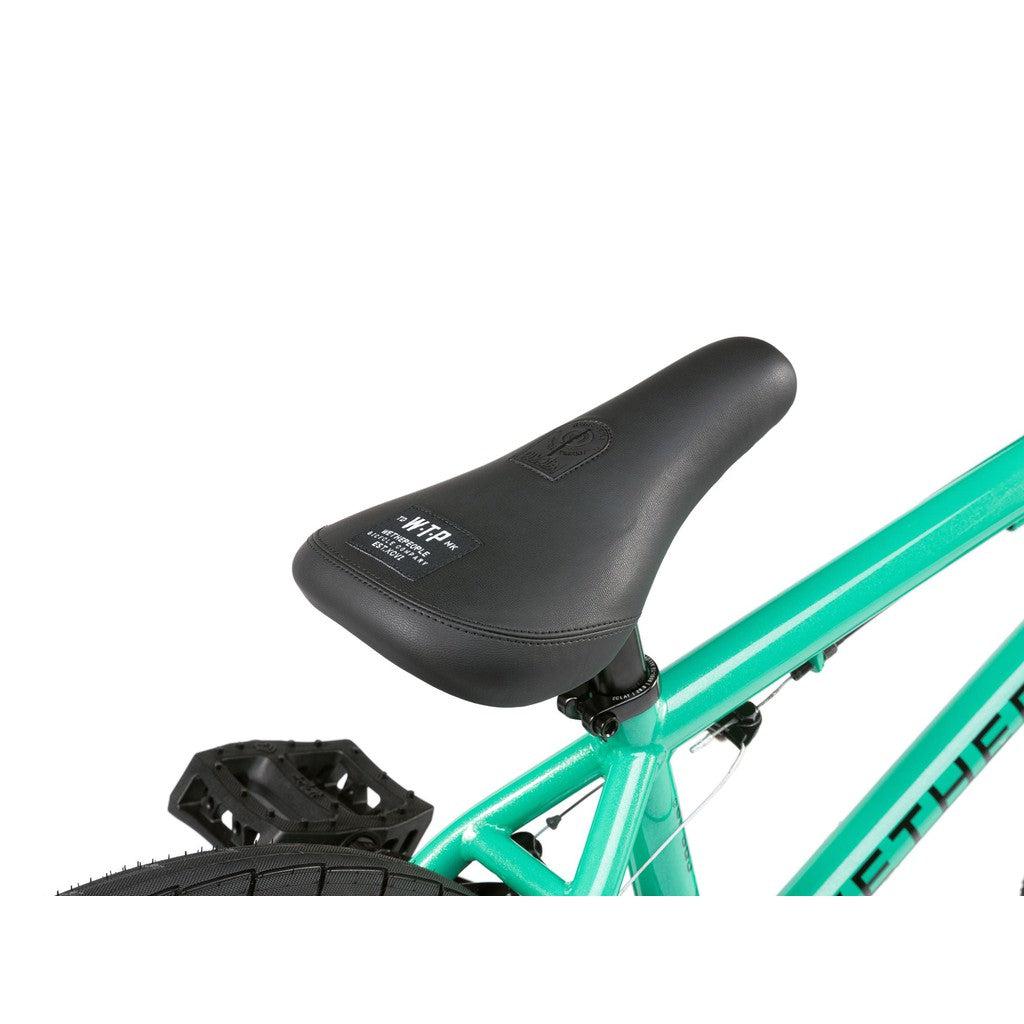 Close-up of a black bicycle seat attached to the green frame of a Wethepeople CRS FS 18 Inch BMX Bike, partially showing the back tire and pedal.