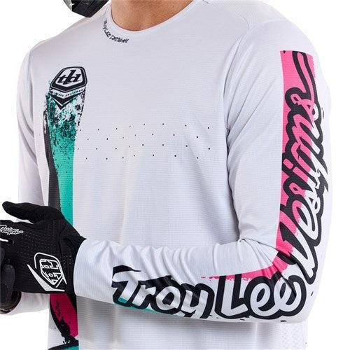 Wearing a TLD 25.1 Sprint Jersey in Full Pull Chalk, adorned with colorful graphics and "Troy Lee Designs" text on the sleeve, ideal for race weekends, complemented by black gloves.