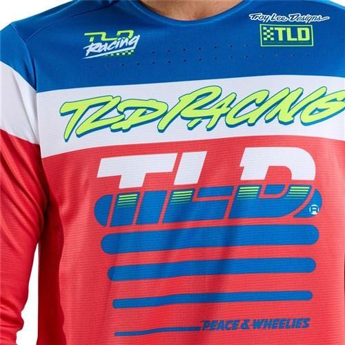 A person in a TLD 25.1 Sprint Jersey / Fifty-50 Fiery Red from Troy Lee Designs, showcasing "TLD Racing," "TLD," and "Peace & Wheelies," gears up for thrilling race weekends.