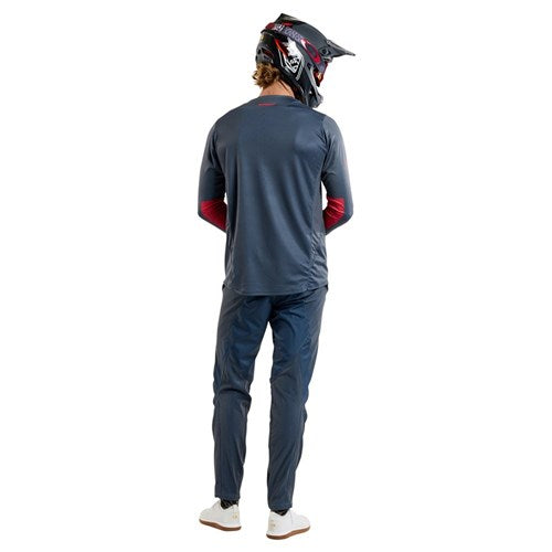 Dressed in a TLD 25.1 Sprint Jersey / Mono Steel Blue, a person in a bike helmet and dark outfit stands with their back to the camera in a studio, ready for race weekends.