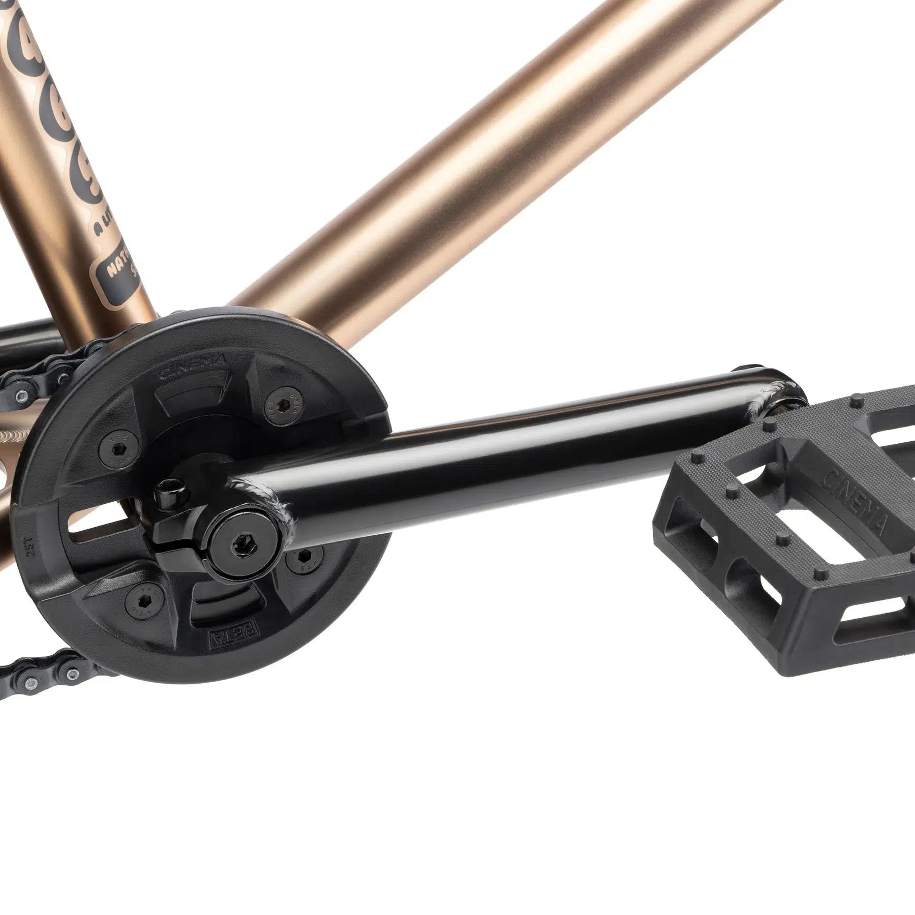 Close-up of the Kink Williams 20 Inch Bike's black crankset and pedal attached to its metallic bronze frame.