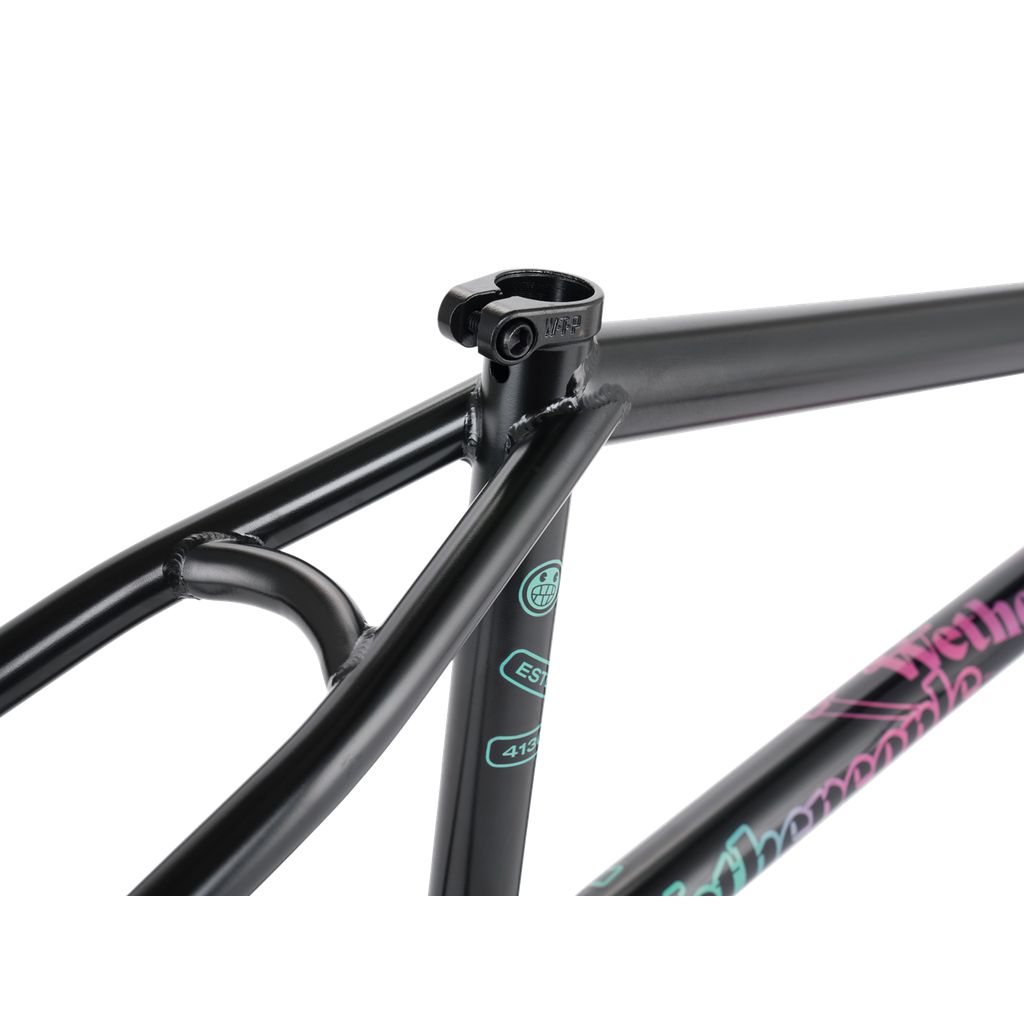 Close-up of the Wethepeople Trigger Frame, a durable black bicycle frame highlighting intricate welds and colorful decals, featuring adaptive geometry with the seat post mount at the top.