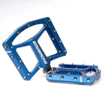 A pair of blue Stay Strong FORCE Pro Platform Pedals with a sleek design and metal pins for grip, displayed against a white background.