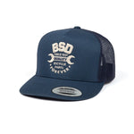 The BSD Workshop Trucker Hat, featuring a navy blue snapback design with a breathable mesh back, displays the text "BSD Quality Bicycle Parts Forever" alongside two wrench graphics and "Since 1991.