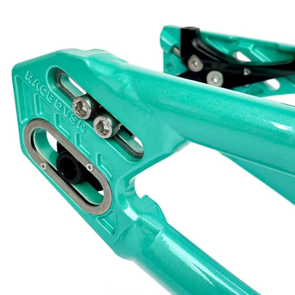 Close-up of a turquoise Staystrong V5 Disc Pro XL Frame with metal hardware and the "RACE DSN" engraving, highlighting parts of the suspension linkage alongside a robust disc brake system.