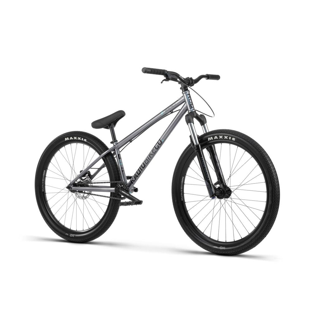 A silver Radio 26 Inch Asura Pro Bike with a black seat, black handles, and black Maxxis tires, featuring a sturdy dirt jump frame and hydraulic disc brakes, displayed on a white background.