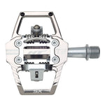 The HT T2-SX Clip In Pedals are sleek, silver pedals featuring a spiked platform and a central spring mechanism. Boasting CNC-machined precision and sealed bearings for durability, the clipless design proudly displays the letters "SX" and "T2" on its metallic body.