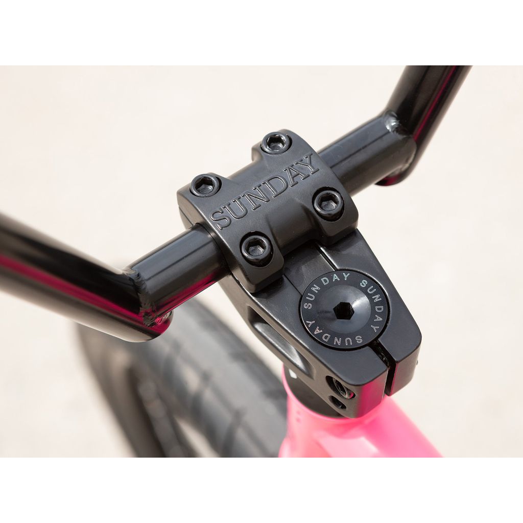 Close-up of a black handlebar stem on the Sunday Street Sweeper 20 Inch Bike, attached to a pink chromoly frame with "Sunday" branding.