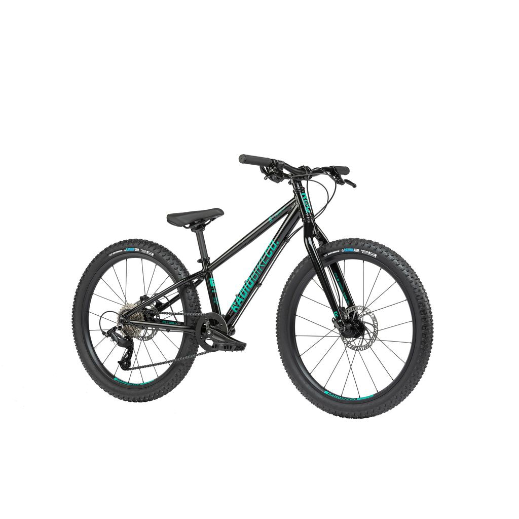 The Radio 24 Inch Zuma Bike is a black mountain bike with teal accents, featuring a sturdy, lightweight alloy frame, flat handlebars, a cushioned seat, and large knobby tires designed for off-road cycling.