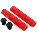 Two red ribbed, flangeless Alienation Backlash V2 bicycle handlebar grips with black bar end plugs rest on a white background. Made from a proprietary formula rubber, they promise style and durability.