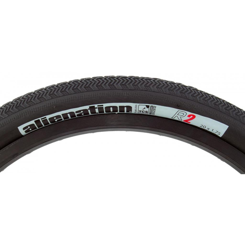 Close-up of a black bike tire with a directional pattern and textured tread. The sidewall reads "alienation R2 20 x 1.75," indicating its Tubeless Compatible System. This Alienation TCS R2 Tyre offers enhanced performance and reliability on varied terrains.