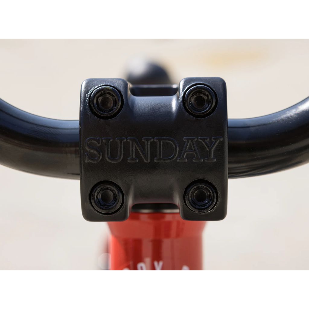 Close-up view of a BMX bike handlebar stem with the word "SUNDAY" embossed on it. The stem is bolted and appears mounted on a red Sunday Primer 18 Inch Bike (2025) frame.