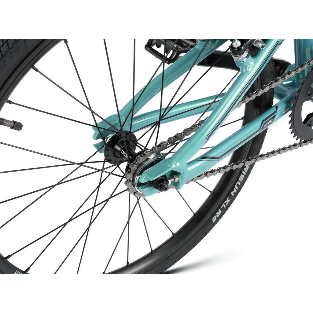 Close-up image of the rear wheel and gear mechanism of a teal BMX race bike, showing the chain, spokes, tire, and frame from Radio Cobalt Expert Bike.