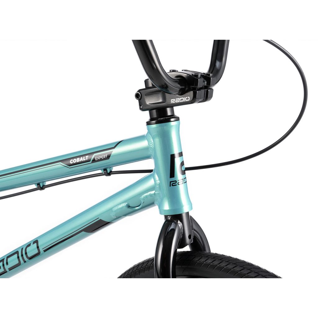 Close-up of a teal-colored bicycle frame with the word "Radio Cobalt Expert Bike" on it, featuring black handlebars and brake cables, and a visible section of the front tire. This BMX race bike is perfect for those seeking an entry level ride to kickstart their racing journey.