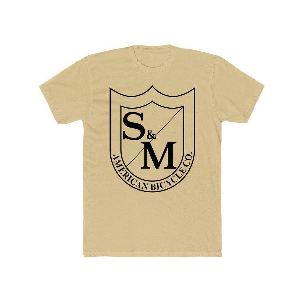 Introducing the S & M Big Shield T-Shirt, a beige tee featuring an oversized shield design on the front adorned with "S&M" and "American Bicycle Co." Made from 100% combed ring-spun cotton, it offers ultimate comfort and style.