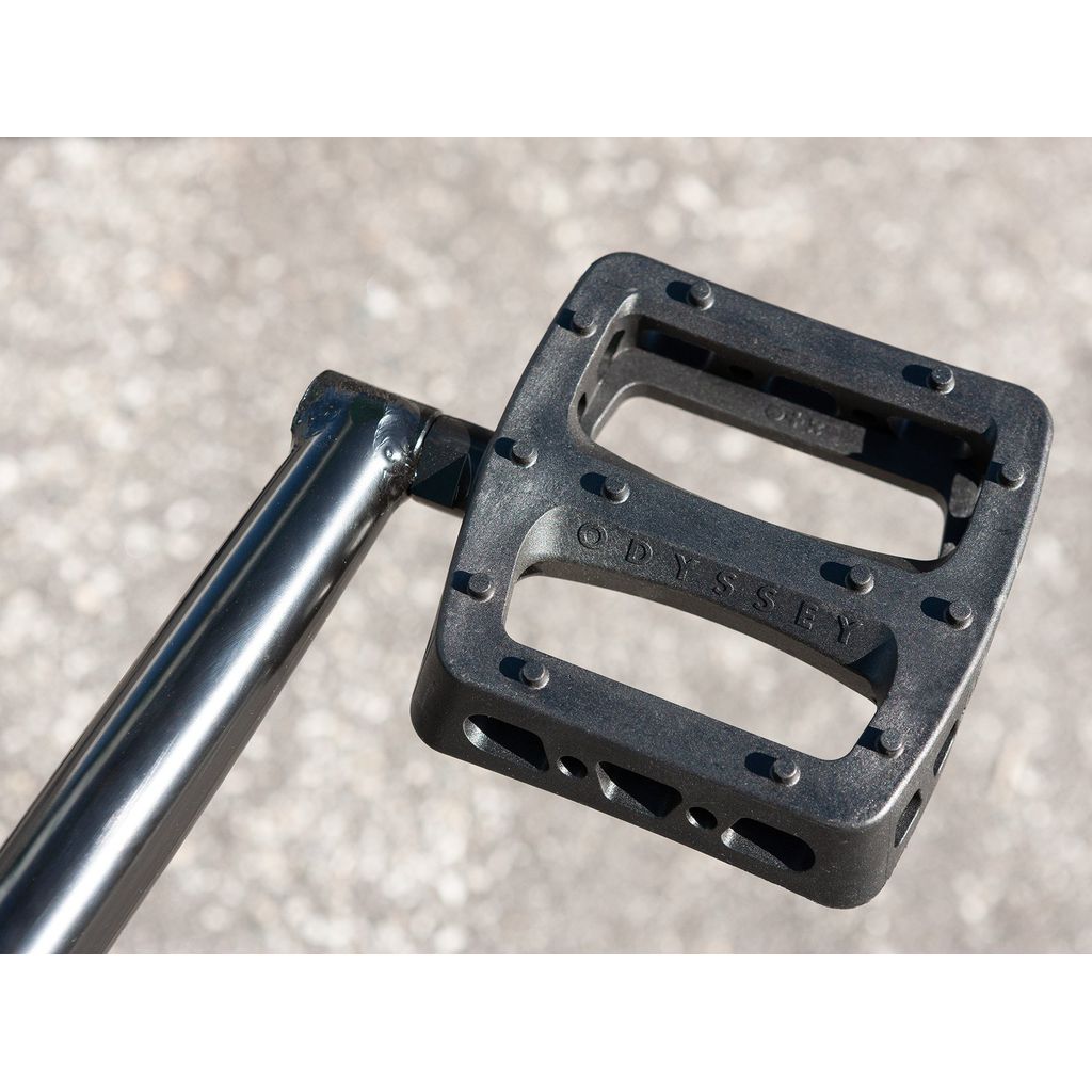 Close-up of a black Odyssey bicycle pedal attached to a crank arm, mounted on a Sunday Forecaster 20 Inch Bike (2022) / Alec Siemon with a 100% chromoly frame. The background is blurred pavement.