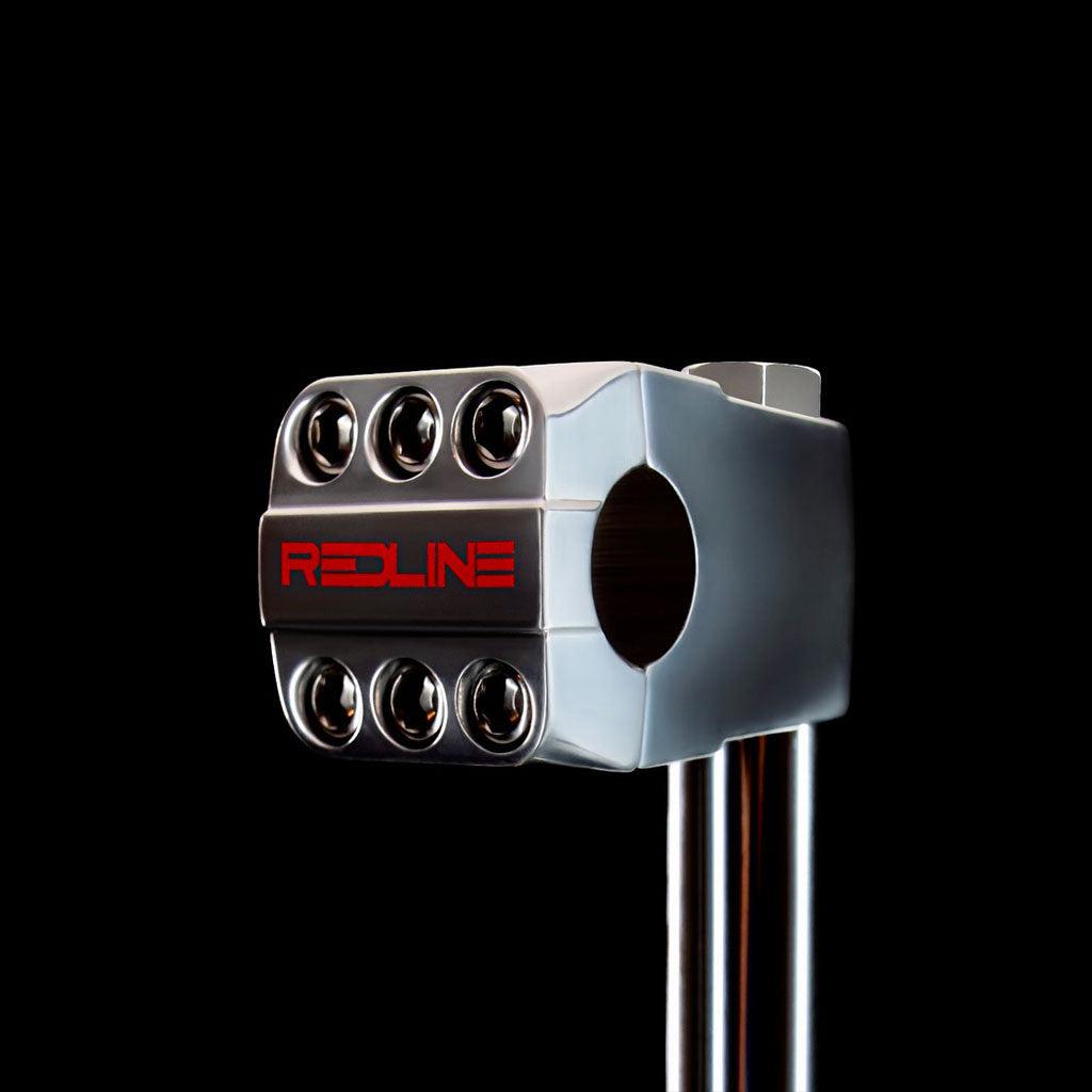 Close-up of a metallic component against a black background, featuring six visible bolts and the word "REDLINE" printed in red. This limited edition stem is part of the RL22 build, known as the REDLINE BY KASTAN Forklifter 6 Bolt F/Load Stem.