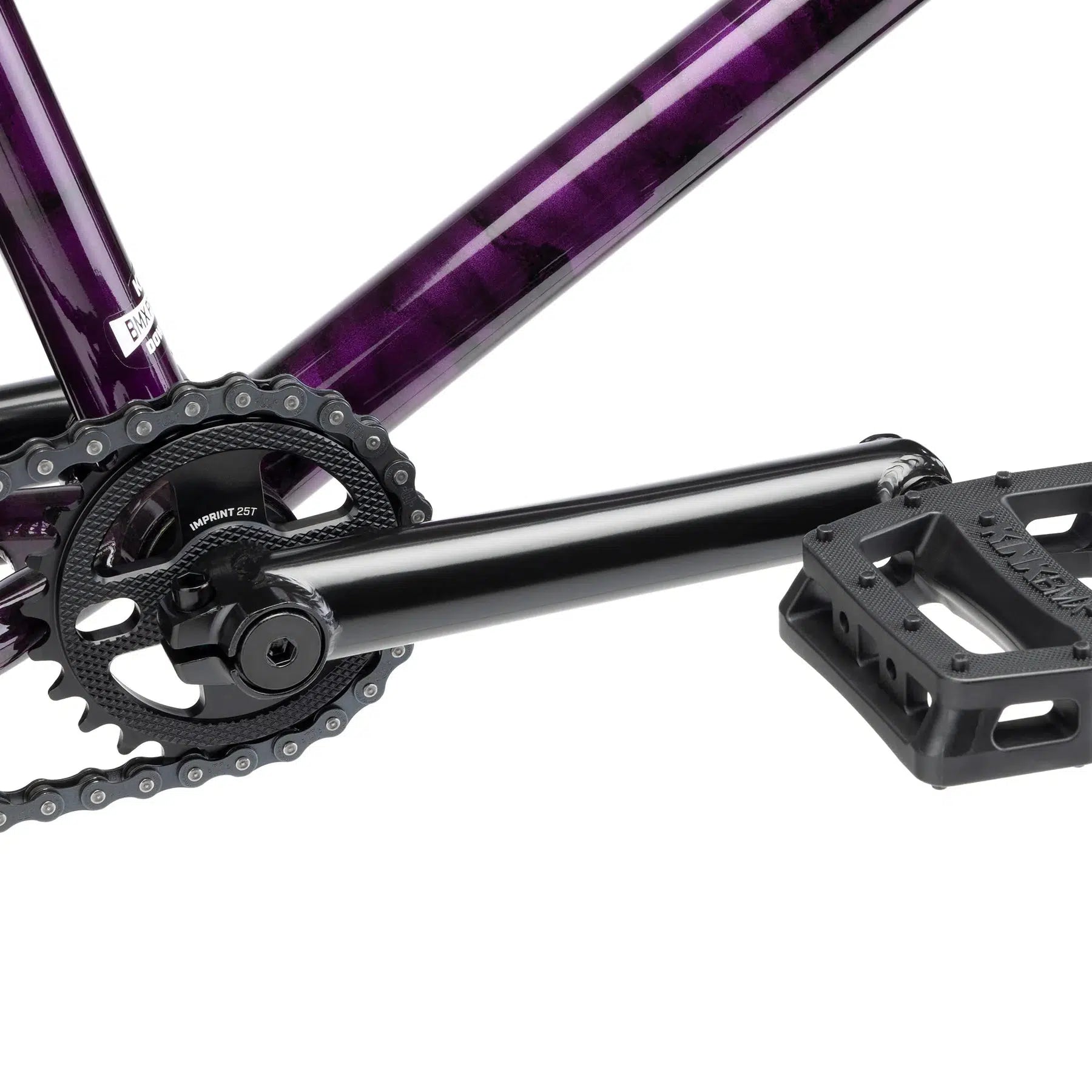 Close-up of a bicycle's chainring, crank arm, and pedal, with a purple frame in the background. The chain is not visible. This Kink Downside 20 Inch Bike features modern geometry and quality aftermarket parts.