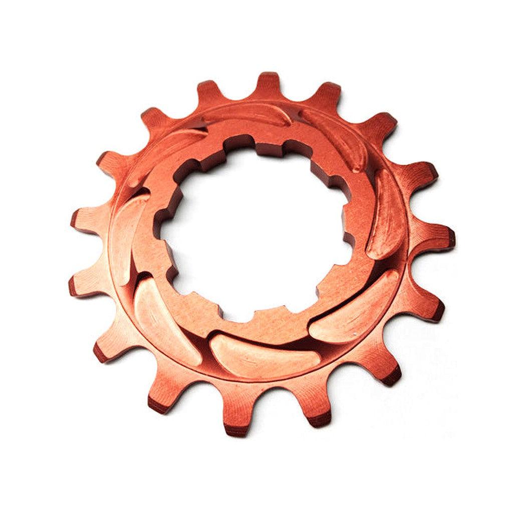 A bronze gear-like metal object, crafted from 7075-T6 Aluminium with twelve teeth and circular grooves, shown on a white background. This Rennen Alloy Cog boasts a single speed specific tooth profile for optimal performance.