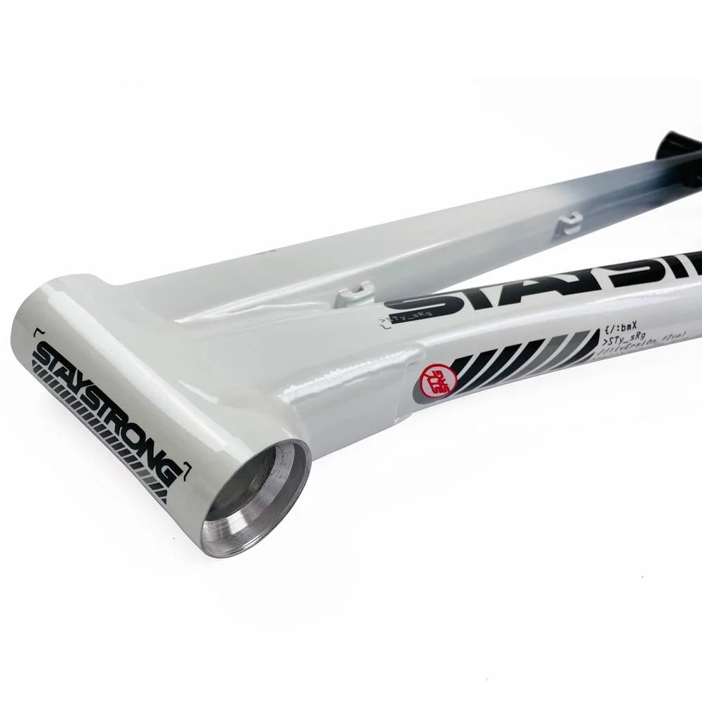 Close-up shot of a white BMX bike frame with "STAYSTRONG" and stickers on the aluminium race frame. The Staystrong V5 Disc Junior Frame features a bottom bracket shell and part of the top tube.