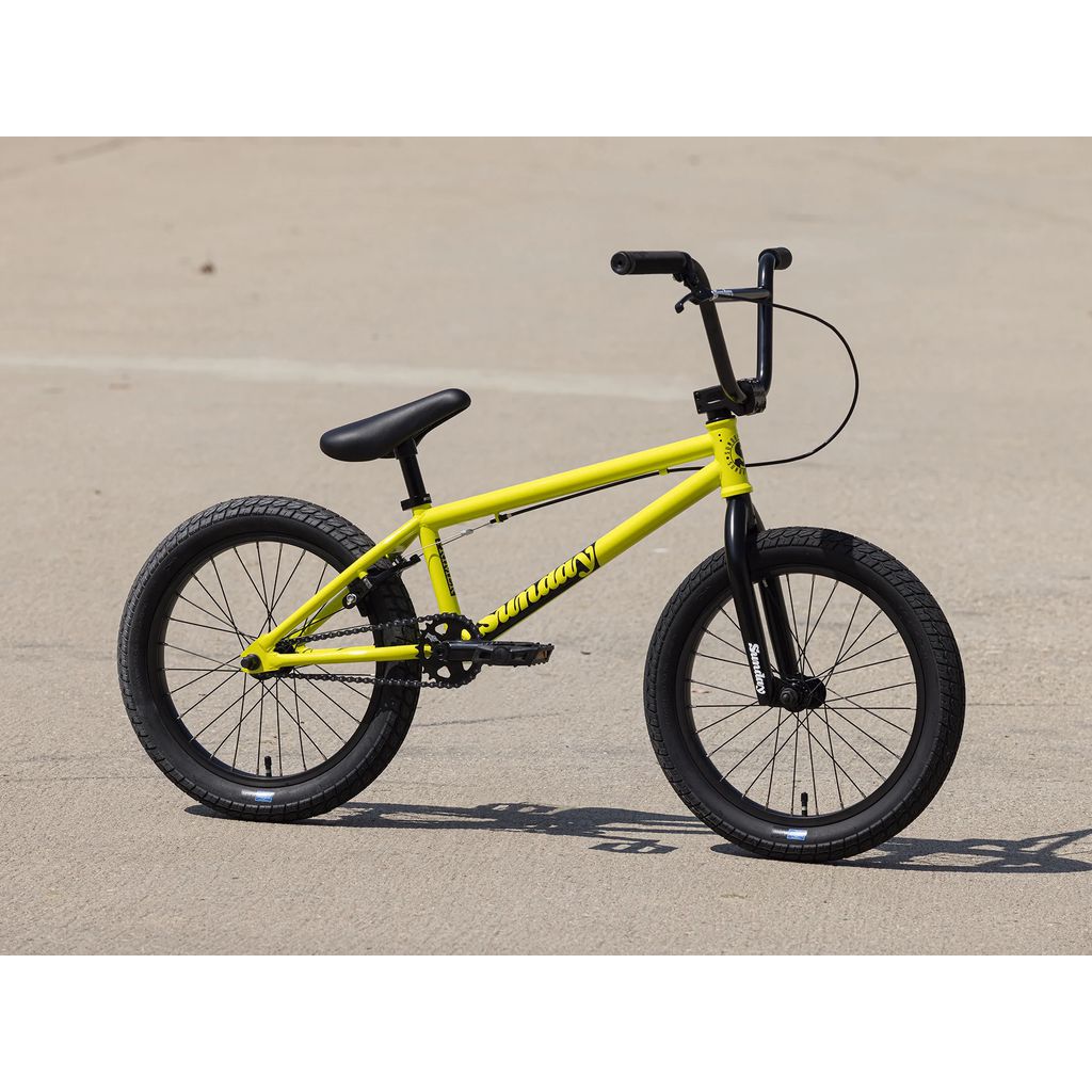 A 2025 Sunday Primer 18 Inch BMX bike in yellow on a paved surface, featuring a black seat, handlebars, Odyssey Springfield brakes, and tires.