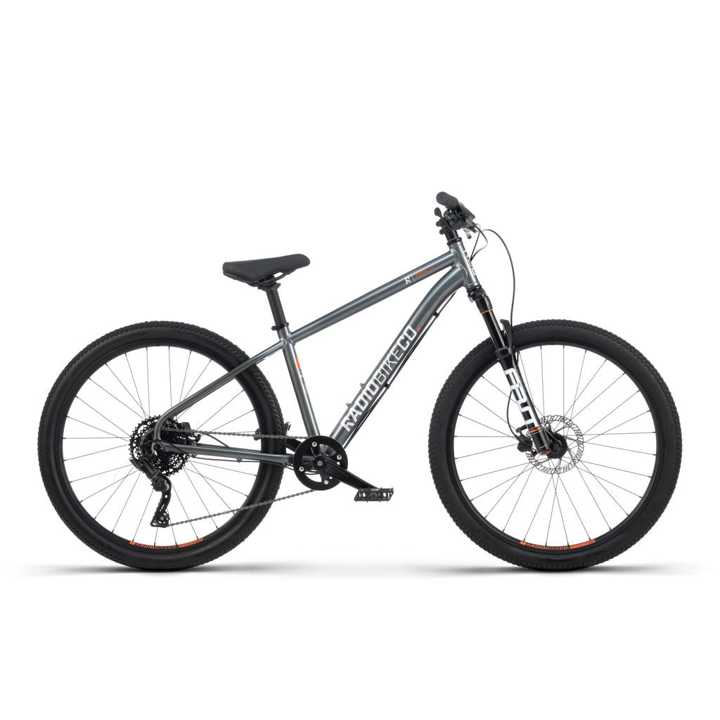 A side view of the Radio 26 Inch Zuma Sus Bike, featuring a grey and black color scheme, lightweight alloy frame, front suspension fork, disc brakes, and knobby tires.